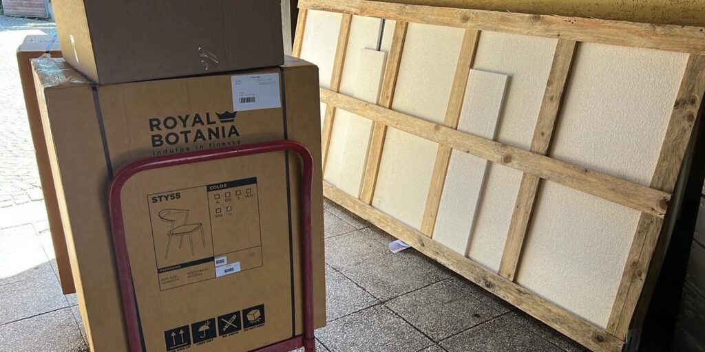 Vrtni stoli v kartonski embalaži in velika mizna plošča v zaščitnem lesenem transportnem okvirju.